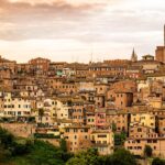 Vista panoramica di una città toscana con vigneti e turisti che degustano vino.