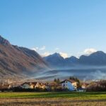 Panorama montano con cielo azzurro, case tradizionali e natura incontaminata nel paese descritto nell'articolo.
