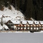 Vista panoramica del lago di Braies con turisti, contrasto con un lago deserto e sereno in lontananza.