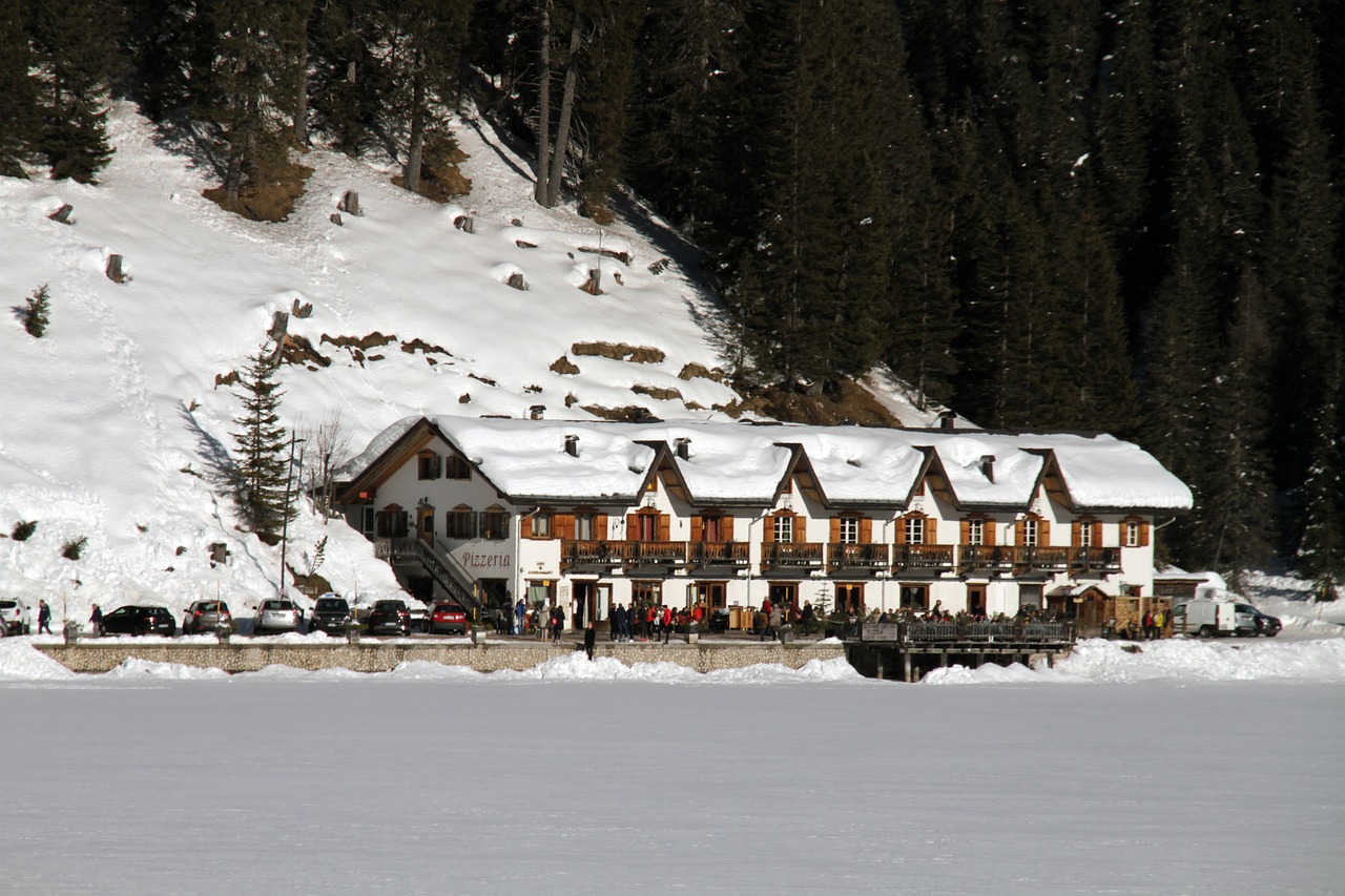Vista panoramica del lago di Braies con turisti, contrasto con un lago deserto e sereno in lontananza.